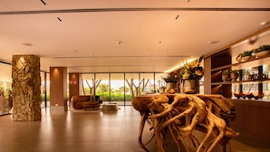A spacious lobby with a central wooden sculpture, a stone pillar, and a seating area with a view of greenery outside. - Amazon Aeroporto Hotel (Varzea Grande)