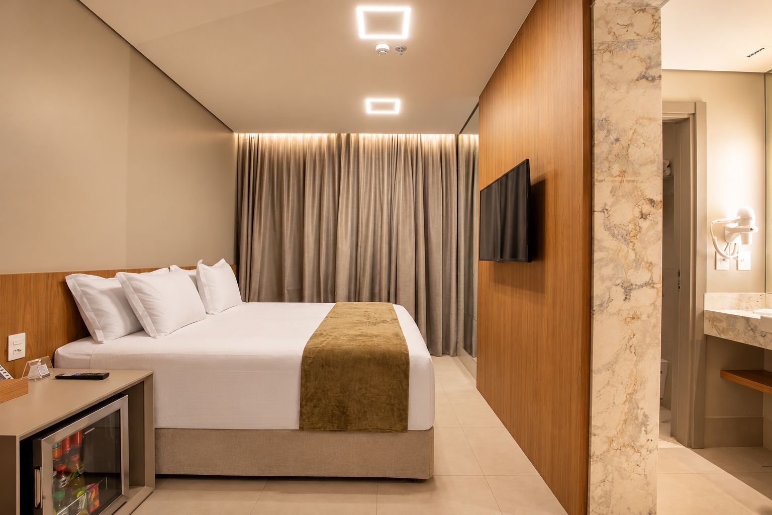 A hotel room with a bed, a television, a desk with a phone, and a bathroom with a mirror and sink.