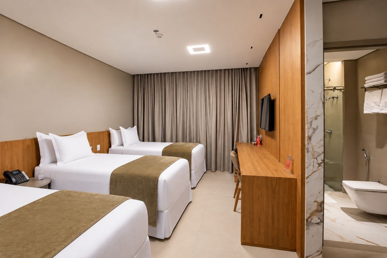 Habitación de hotel con dos camas, un escritorio, un televisor y un baño con ducha y lavamanos.
