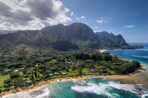 An aerial view of a coastal resort with lush greenery, a beach, and a mountainous backdrop. - Princeville Gem, Walk to Beaches, Shopping/Dining (Princeville)
