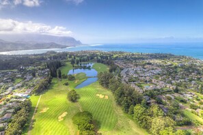 A golf course with a pond, houses, and a view of the ocean.