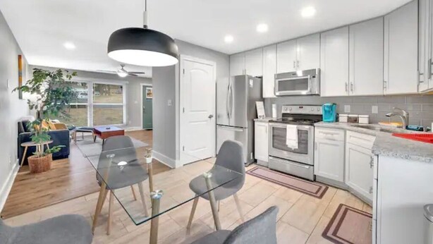 Una cocina moderna con armarios blancos, electrodomésticos de acero inoxidable y una mesa de comedor de vidrio.