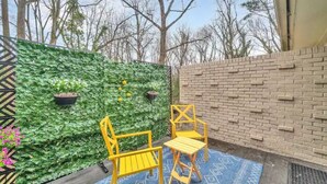 Un patio con muro de ladrillo, pared verde con plantas y dos sillas amarillas.
