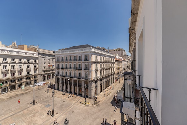 A view of a city square with historic buildings, a clear sky, and pedestrians.