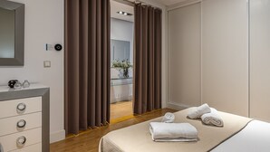 Camera moderna con un letto, una cassettiera, uno specchio e un bagno parzialmente visibile attraverso una tenda.
