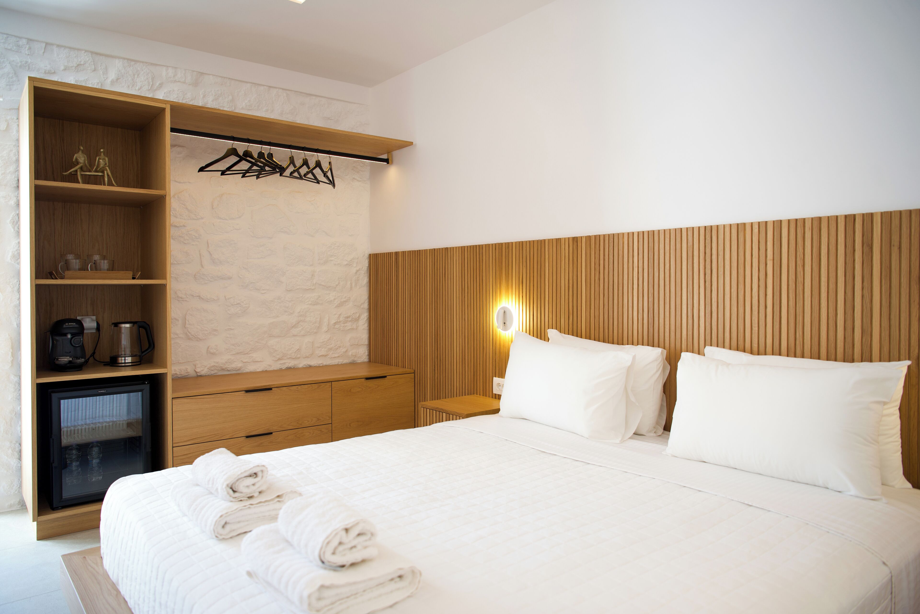 Une chambre d’hôtel comprenant un lit, une armoire en bois, un petit réfrigérateur et un luminaire fixé au mur.