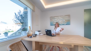 A modern office with a wooden desk, a laptop, and a window with a view of the outdoors. - Elit Suites Mykonos (Mykonos)