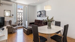 A modern living room with a dining area, a television, and a large window with a view of buildings.