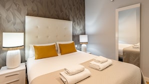A hotel room with a tufted headboard, two bedside lamps, a large mirror, and neatly folded towels on the bed.