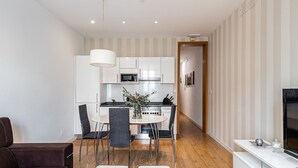 A modern kitchen with white cabinets, a microwave, and a stove. There is a dining area with a table and chairs, and a TV on a stand.