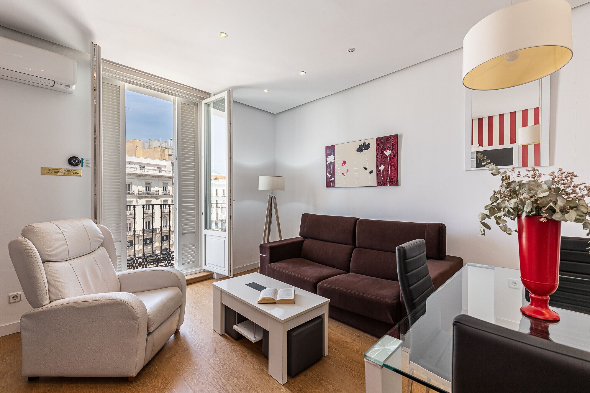 A modern living room with a sofa, armchair, coffee table, and a red vase with flowers.