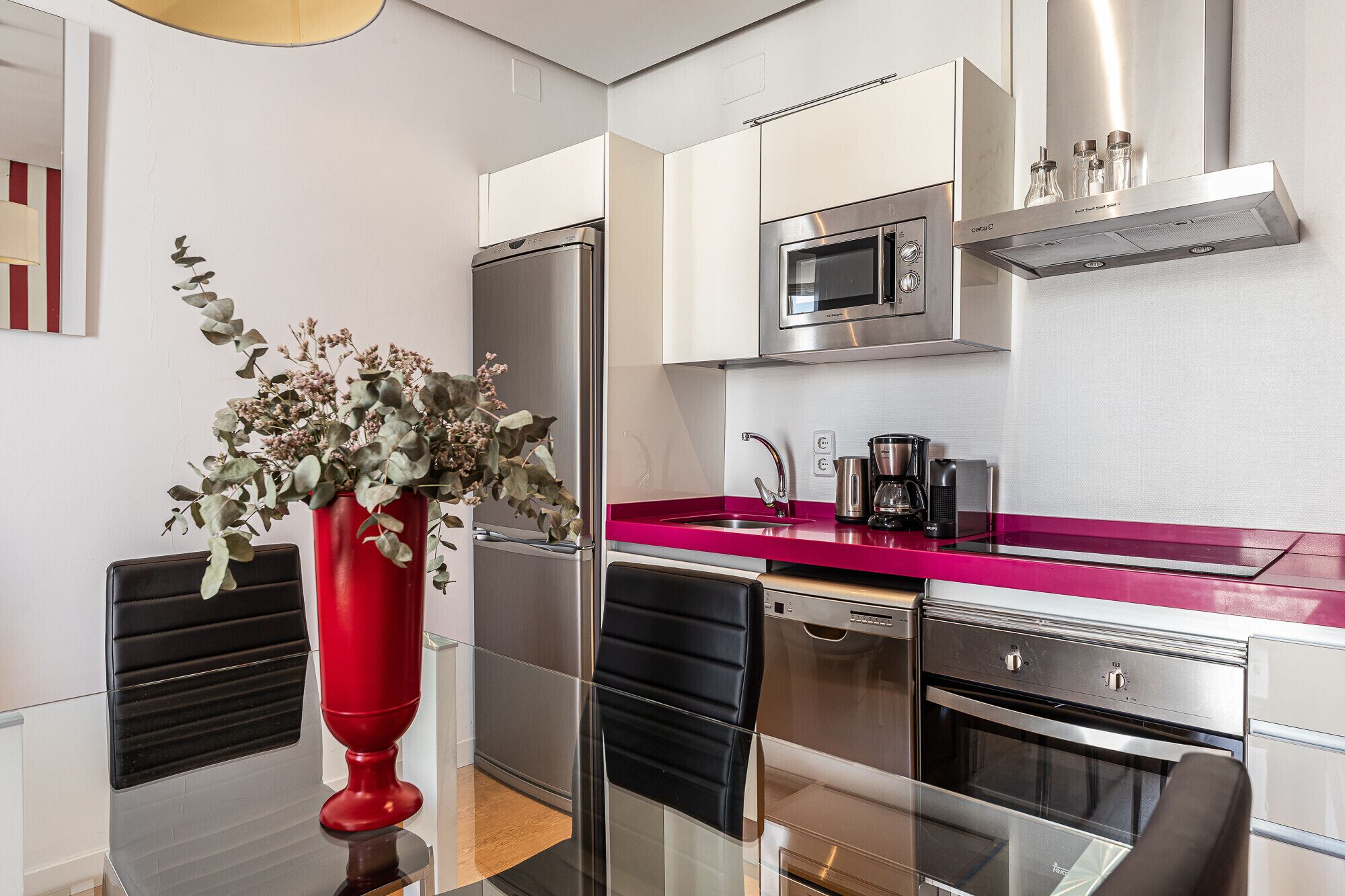 Et moderne køkken med rustfrie hårde hvidevarer, en rød bordplade og en vase med blomster.