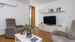 Un saló modern amb un televisor de pantalla plana, dos sofàs grisos, una taula de cafè blanca i un vas de vidre amb flors.