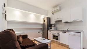 Una cucina compatta con forno a incasso, microonde ed elettrodomestici, vicino a una zona salotto con un divano marrone e un tavolino.