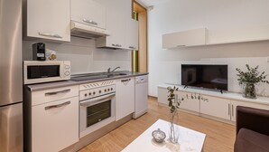 Una cucina moderna con elettrodomestici in acciaio inossidabile, forno integrato e microonde. Una porta in legno dà accesso a un'altra stanza, e c'è un televisore montato a parete.