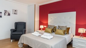 A modern hotel room with a large bed, a grey armchair, and a red accent wall. - Waou Apartamentos en Sol Confort 6 (Madrid)