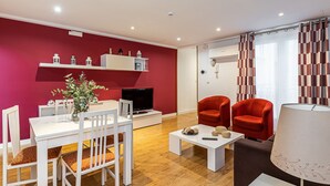 A modern living room with a red accent wall, a dining area with white furniture, and a cozy seating area with red chairs. - Waou Apartamentos en Sol Confort 6 (Madrid)
