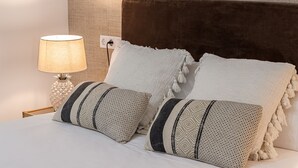 A neatly made bed with patterned pillows, a lamp, and a power outlet on the wall. - Waou La Latina IV - Alquiler Corta Duración (Madrid)