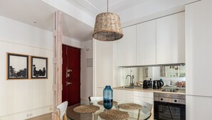 A modern kitchen with a glass dining table, white cabinets, and a red door. - Waou La Latina IV - Alquiler Corta Duración (Madrid)