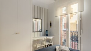 A bedroom with a bed, a desk, and a chair. There is a balcony with a view of a building. - Waou La Latina IV - Alquiler Corta Duración (Madrid)