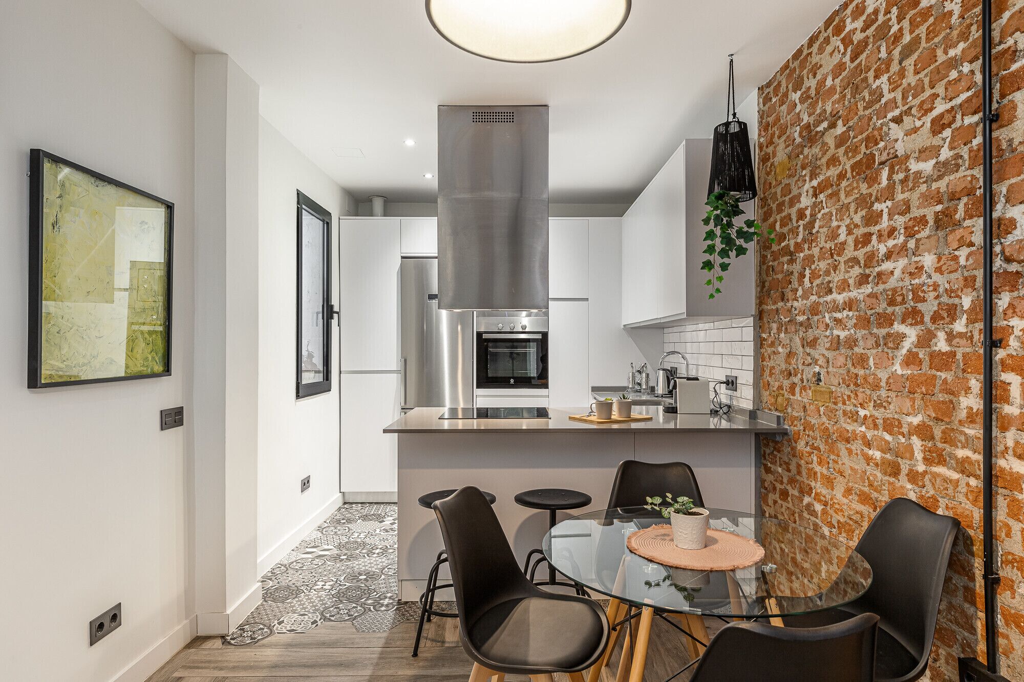 Een moderne keuken met roestvrijstalen apparatuur, een glazen eettafel en zwarte stoelen.