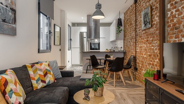 A modern living room with a grey sofa, a coffee table, and a dining area with chairs and a table.