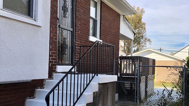 A two-story brick house with a white exterior, a black metal staircase, and a fenced yard. - Sky cozy apartment with rooftop views (Louisville)