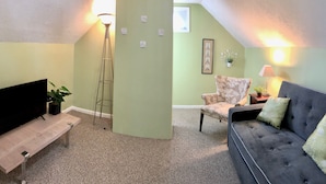 A living room with a TV, sofa, chair, floor lamp, and a small table with a plant. - Sky cozy apartment with rooftop views (Louisville)