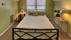 A bedroom with a bed, two bedside tables, a radiator, and a window with blinds. - Sky cozy apartment with rooftop views (Louisville)