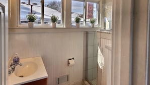 A bathroom with a sink, a toilet, a shower, and three windows with potted plants. - Sky cozy apartment with rooftop views (Louisville)