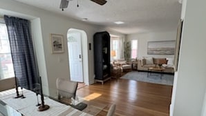 Amplia sala de estar con comedor, pisos de madera, ventilador de techo y vista de la habitación contigua.