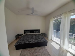 A bedroom with a bed, two bedside tables, a ceiling fan, and a large window with curtains. - SUN AND SEA House (Sosúa)