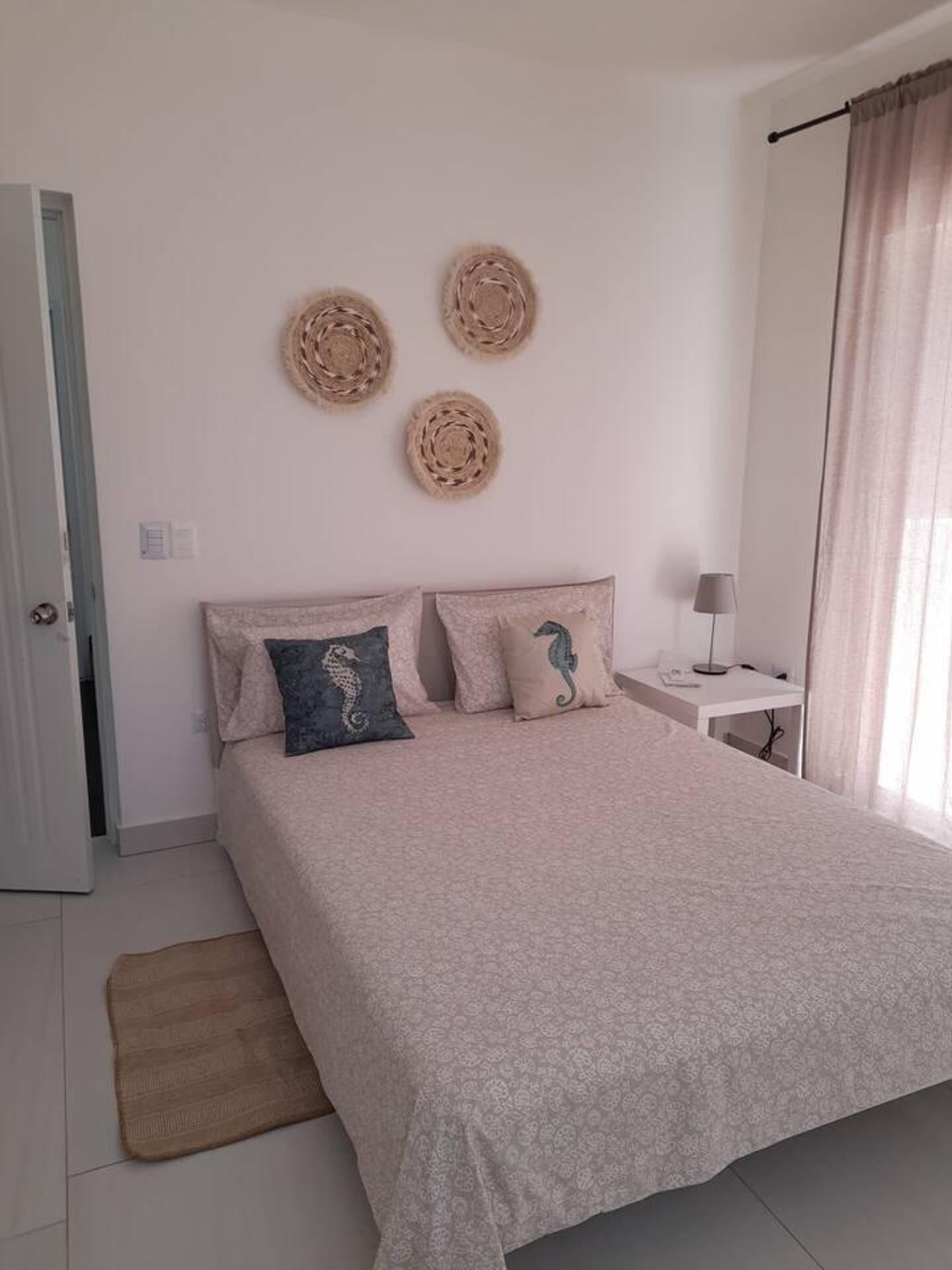 A bedroom with a bed, a bedside table, a lamp, and a door.