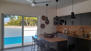 A modern kitchen with a wooden island, black bar stools, and a view of a swimming pool through glass doors. - SUN AND SEA House (Sosúa)