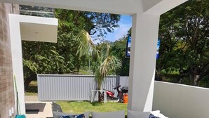 A modern outdoor seating area with a glass table and white cushioned sofa, surrounded by a white wall and a view of a backyard. - SUN AND SEA House (Sosúa)
