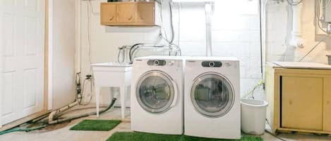 A laundry room with two front-loading washing machines, a small sink, and a cabinet.