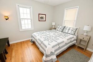 Une chambre à coucher comprenant un lit, deux tables de chevet, une commode, une fenêtre et une porte.