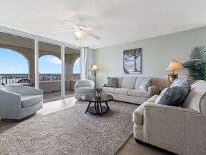 A spacious living room with a large window, a ceiling fan, a sofa set, and a coffee table.