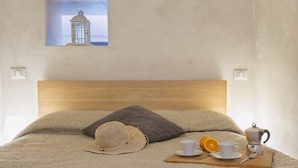 A neatly made bed with a wooden headboard, a decorative wall piece, and a breakfast setup with a cup, orange slices, and a coffee pot.