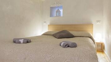 Una cama bien tendida con cabecera, dos almohadas y dos toallas enrolladas.