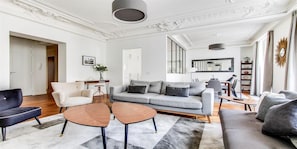 A modern living room with a grey sofa, two wooden coffee tables, and a white armchair.