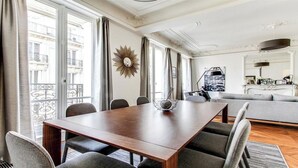 A modern living room with a wooden dining table, grey upholstered chairs, a grey sofa, and a balcony with a wrought iron railing. - TOP OF THE RANGE - CHAMPS ELYSEE LUXE 110M2 (Paris)