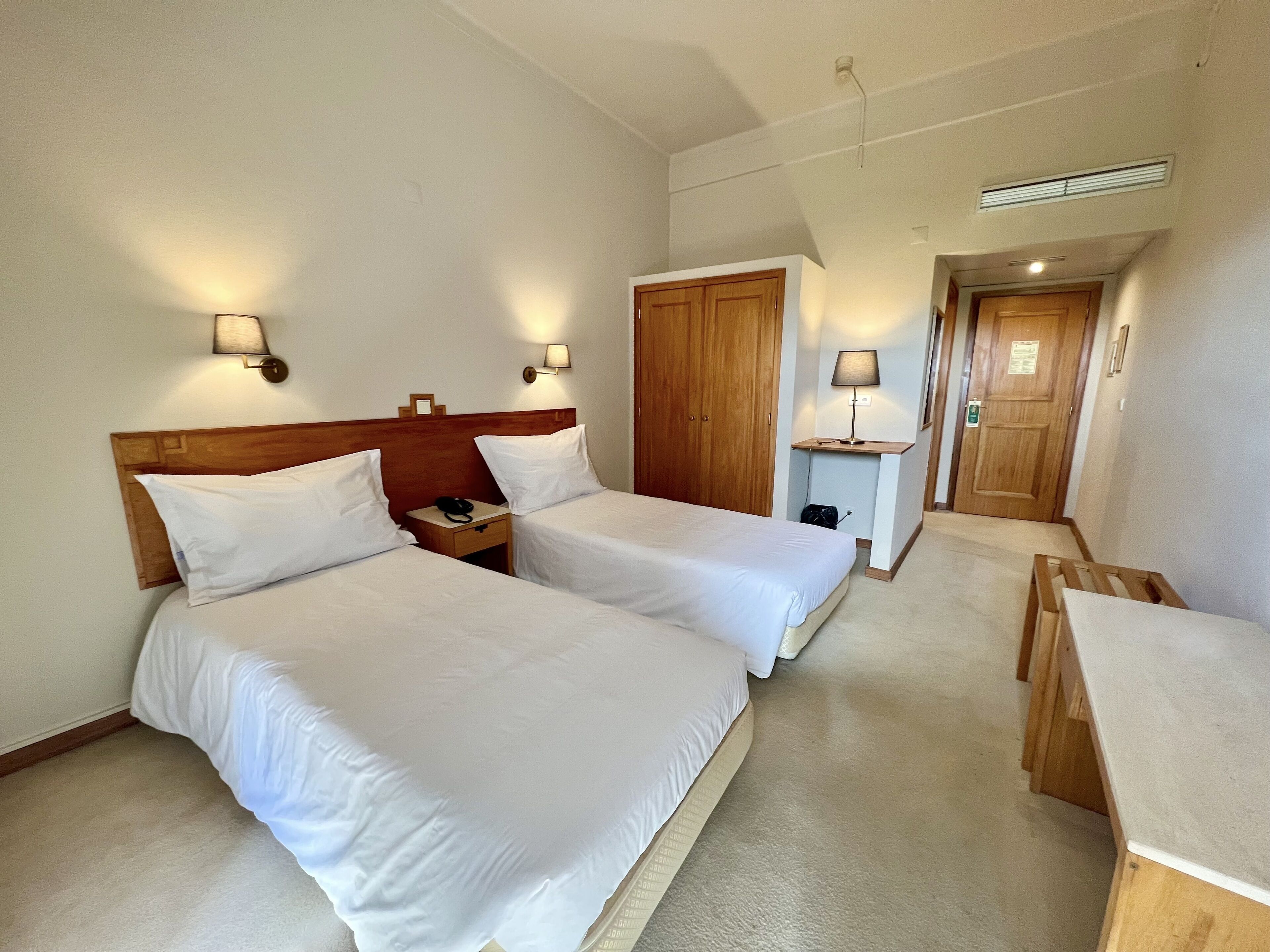 Habitación de hotel con dos camas, cabecero de madera, lámparas de noche, un escritorio y una puerta.