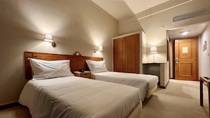 A hotel room with two beds, wooden headboards, bedside lamps, a wooden wardrobe, and a carpeted floor. - Estremoz Hotel (Estremoz)