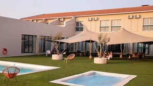 A pool area with two rectangular pools, outdoor seating, and a building with large windows and air conditioning units. - Estremoz Hotel (Estremoz)