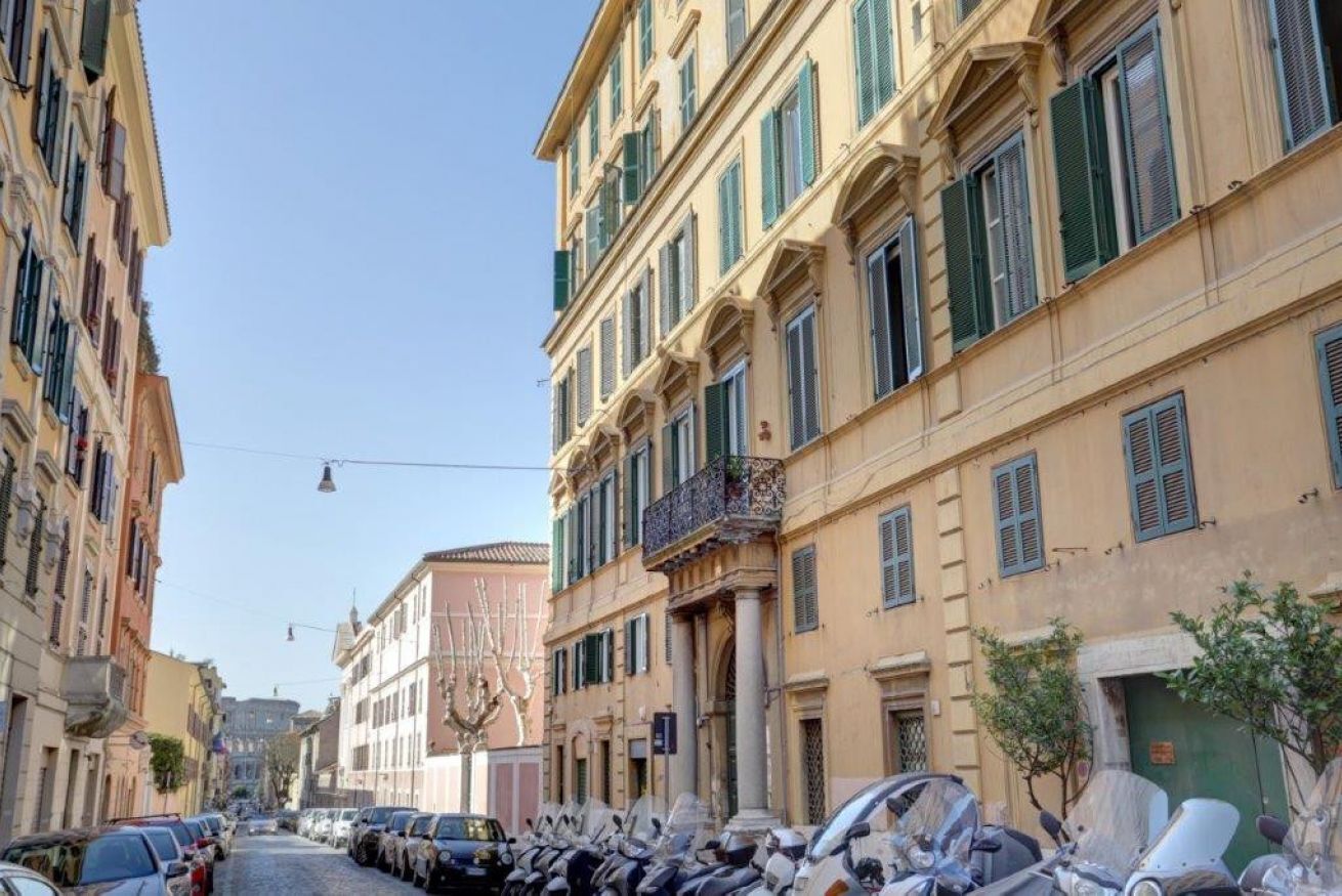 A narrow street lined with parked cars and classic European buildings with green shutters.