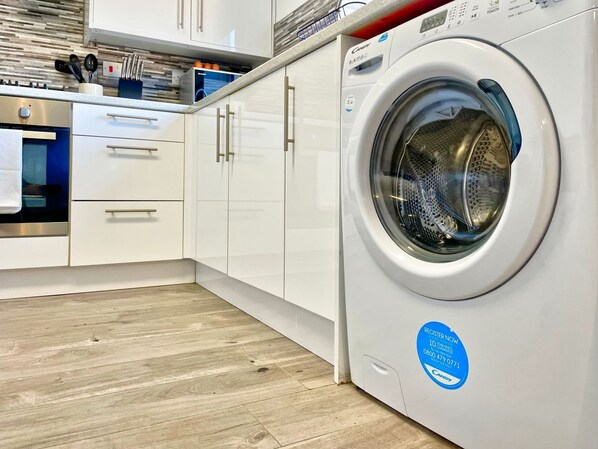 Laundry room with a front-loading washing machine, sleek cabinetry, and stainless steel oven.