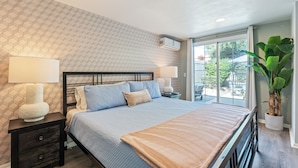 Une chambre à coucher avec un lit, des tables de chevet, des lampes, une grande fenêtre et une plante en pot.