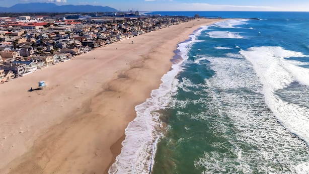 Une ville côtière dotée d’une longue plage, de maisons et d’un ciel bleu azur.