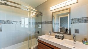 Un bagno moderno con cabina doccia in vetro, un lavandino bianco su mobile contenitore in legno e uno specchio grande.